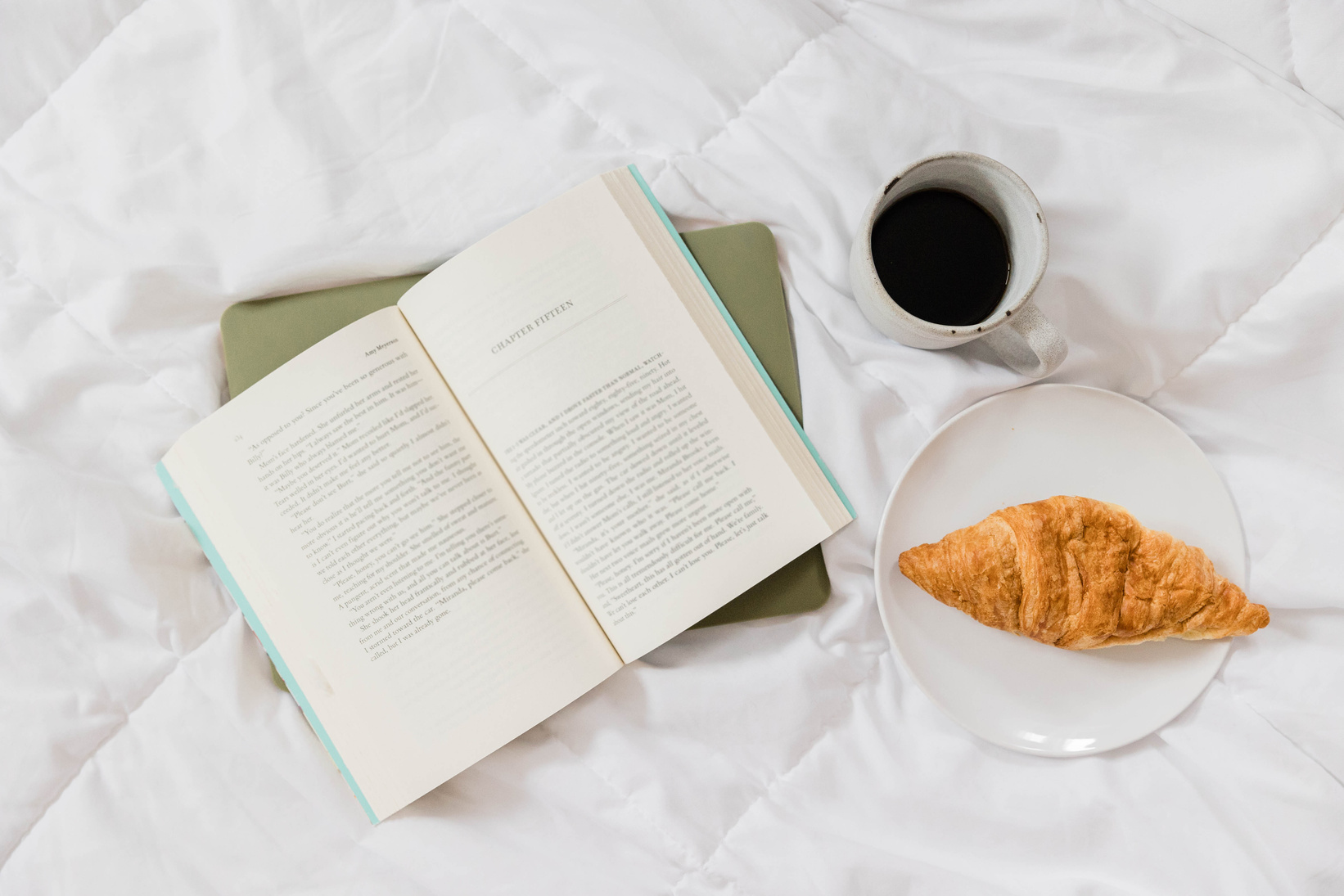 Book with Cup of Coffee and Croissant on Bed